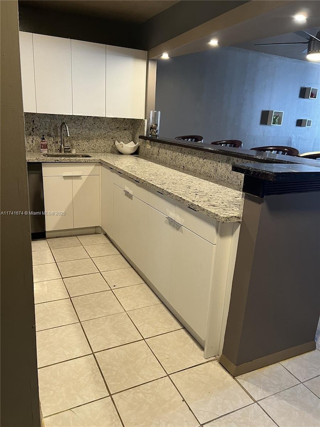 kitchen featuring sink, light stone counters, tasteful backsplash, white cabinets, and light tile patterned flooring