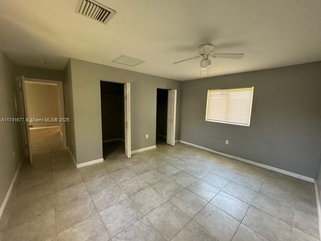 unfurnished bedroom with ceiling fan, light tile patterned floors, and two closets