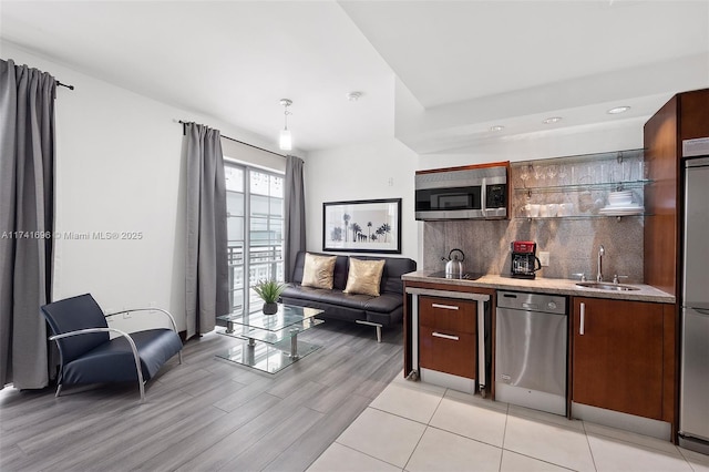 kitchen with decorative light fixtures, sink, decorative backsplash, stainless steel appliances, and light wood-type flooring