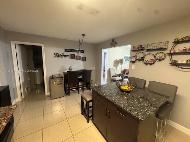 kitchen featuring a breakfast bar area, dark brown cabinetry, washer / dryer, a center island, and light tile patterned floors