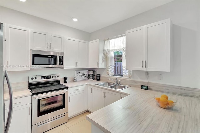 kitchen with appliances with stainless steel finishes, white cabinetry, sink, light tile patterned floors, and kitchen peninsula