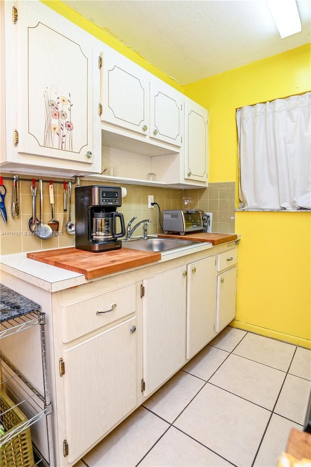 kitchen featuring light tile patterned flooring, backsplash, sink, and white cabinets