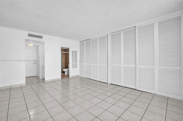 unfurnished bedroom with light tile patterned flooring, two closets, and a textured ceiling