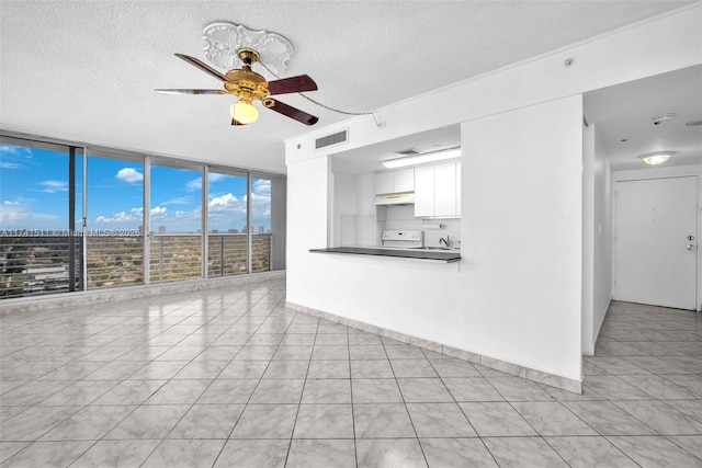 unfurnished living room with sink, light tile patterned floors, ceiling fan, floor to ceiling windows, and a textured ceiling