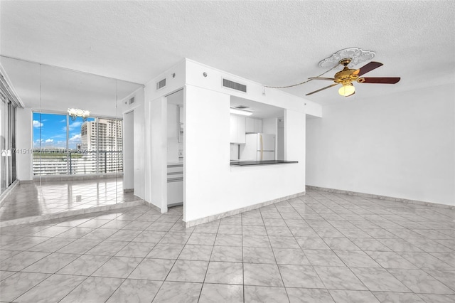 unfurnished living room featuring a wall of windows, ceiling fan with notable chandelier, a textured ceiling, and light tile patterned floors