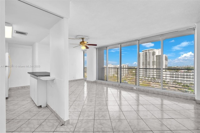 unfurnished room with light tile patterned flooring, ceiling fan, and a wall of windows