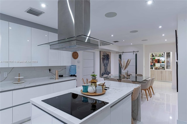 kitchen featuring black electric cooktop, white cabinets, island exhaust hood, a barn door, and backsplash