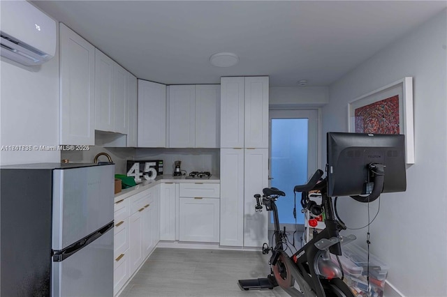 kitchen with a wall mounted air conditioner, stainless steel refrigerator, white cabinets, and light wood-type flooring