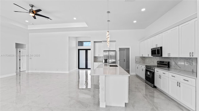 kitchen with appliances with stainless steel finishes, pendant lighting, an island with sink, sink, and white cabinets