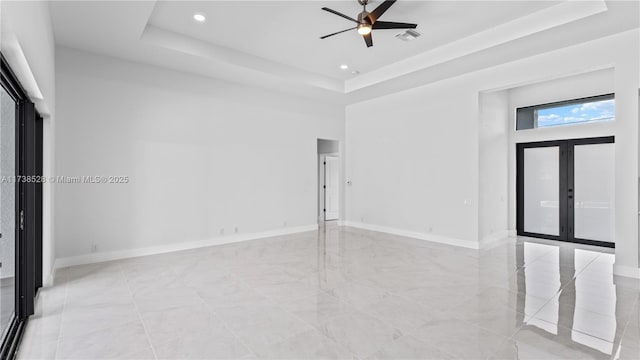 empty room featuring ceiling fan, a raised ceiling, a high ceiling, and french doors