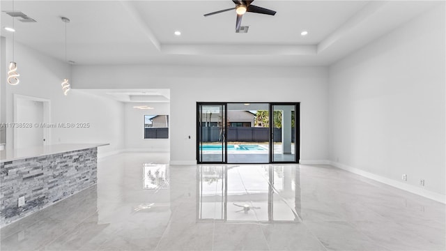 empty room with a towering ceiling, a raised ceiling, and ceiling fan