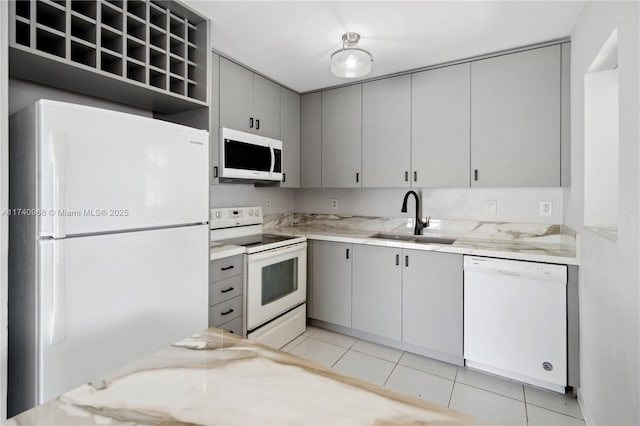 kitchen with light tile patterned flooring, sink, gray cabinetry, light stone countertops, and white appliances