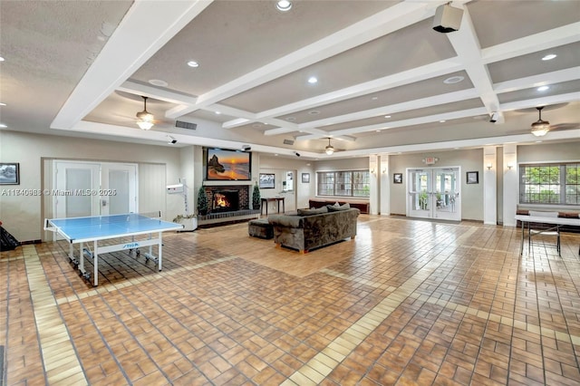 rec room with a brick fireplace, beam ceiling, french doors, and ceiling fan