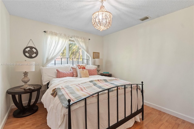 bedroom with a notable chandelier, a textured ceiling, and light wood-type flooring