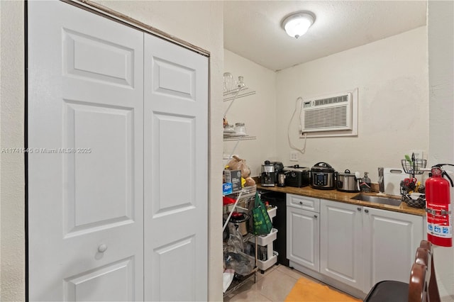 kitchen with light tile patterned flooring, a wall mounted air conditioner, sink, and a textured ceiling