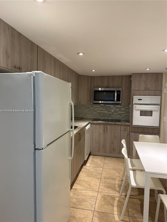 kitchen with light stone counters, light tile patterned floors, white appliances, and decorative backsplash