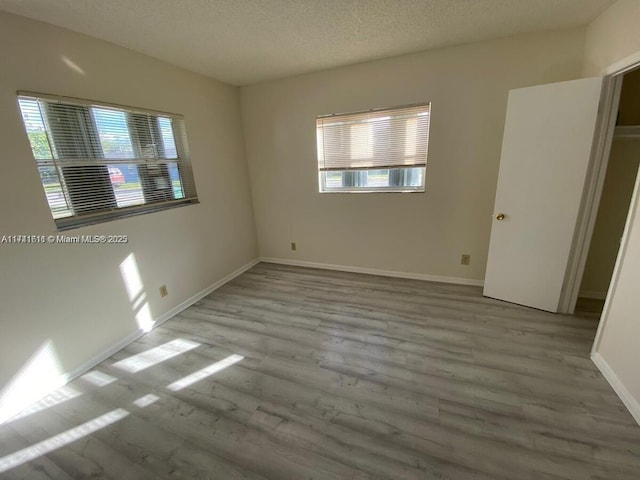 unfurnished bedroom featuring multiple windows, a textured ceiling, and light wood-type flooring