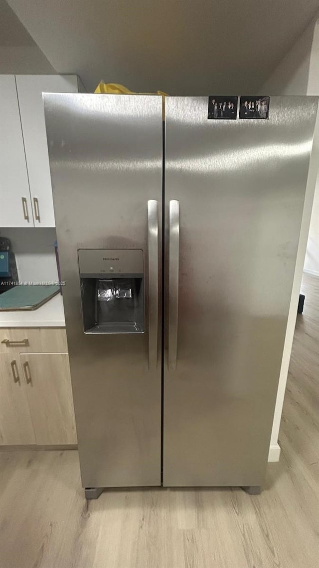 interior details with white cabinets, light wood-type flooring, and stainless steel fridge with ice dispenser