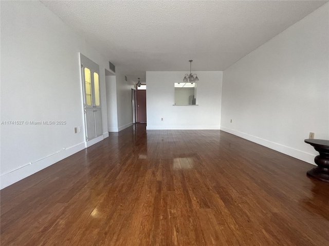 unfurnished living room featuring visible vents, baseboards, a chandelier, a textured ceiling, and dark wood-style flooring