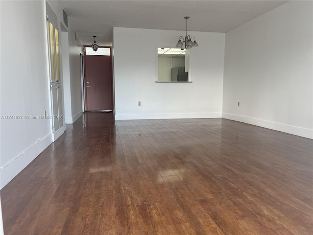 empty room with dark wood finished floors, a notable chandelier, and baseboards