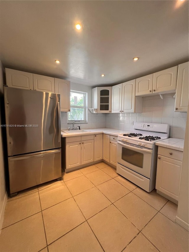 kitchen featuring white gas stove, backsplash, freestanding refrigerator, light tile patterned flooring, and a sink