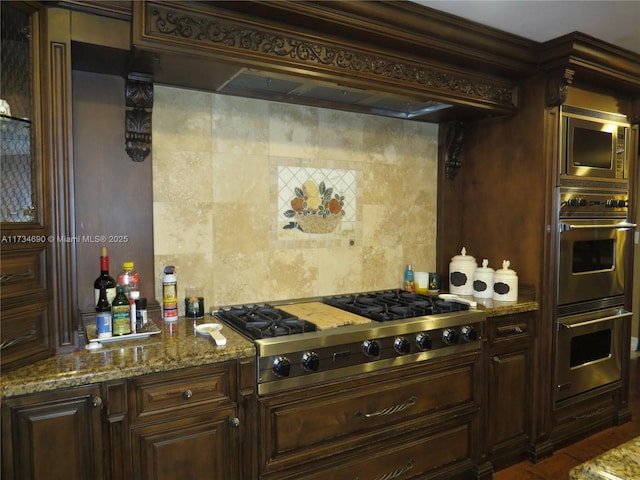 kitchen featuring premium range hood, backsplash, stainless steel appliances, dark brown cabinetry, and light stone countertops