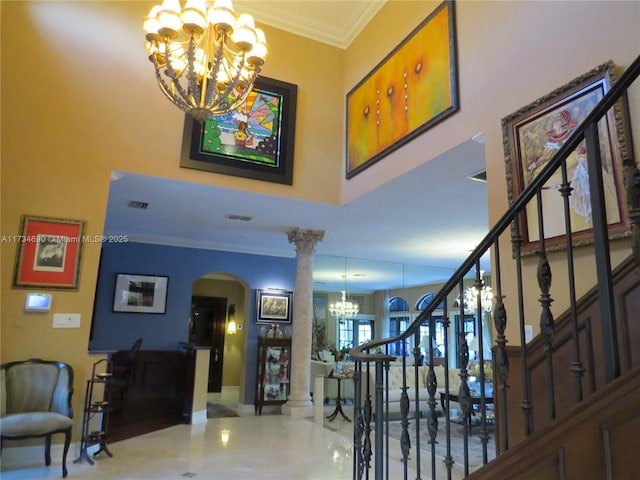 foyer entrance featuring a towering ceiling, ornamental molding, a chandelier, and ornate columns