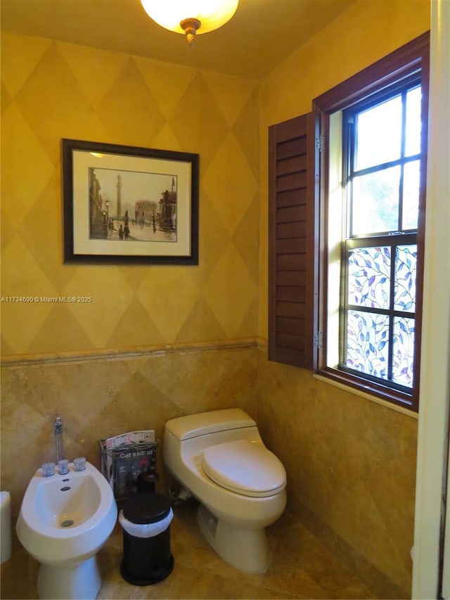 bathroom with a bidet, toilet, and tile walls