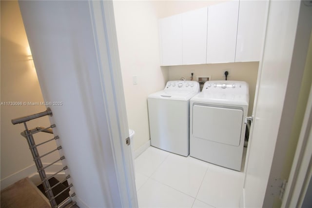 clothes washing area featuring light tile patterned floors, washer and clothes dryer, and cabinets