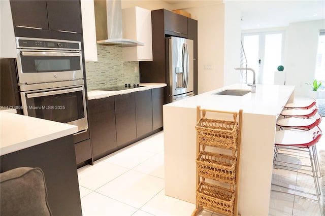 kitchen featuring sink, stainless steel appliances, an island with sink, decorative backsplash, and wall chimney exhaust hood