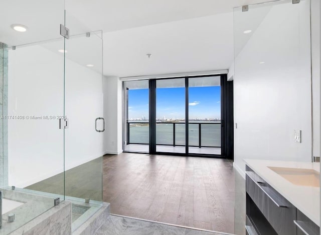 bathroom with expansive windows, vanity, hardwood / wood-style flooring, walk in shower, and a water view