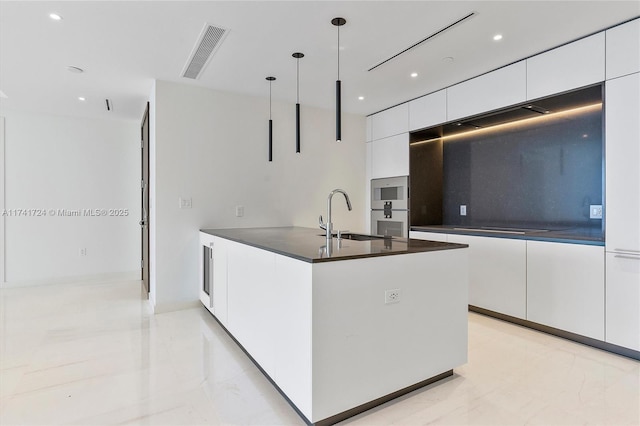 kitchen with pendant lighting, sink, white cabinetry, a kitchen island with sink, and double oven