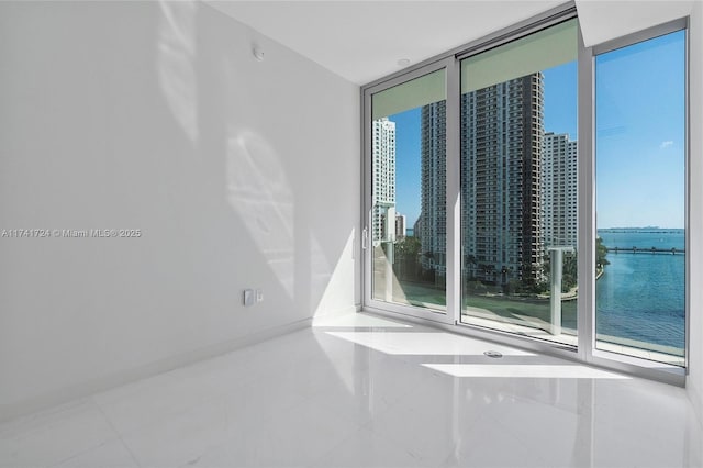 spare room with a water view, a wall of windows, and tile patterned floors