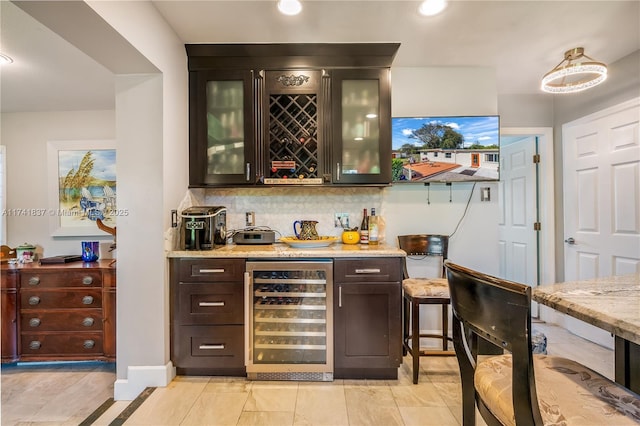 bar featuring beverage cooler, light stone countertops, dark brown cabinets, and backsplash