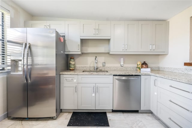 kitchen with stainless steel appliances, white cabinetry, light stone countertops, and sink