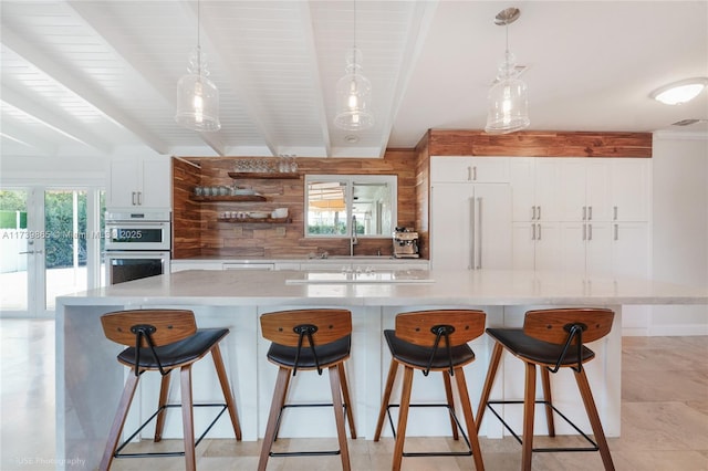 kitchen featuring beamed ceiling, white cabinetry, a large island, and decorative light fixtures