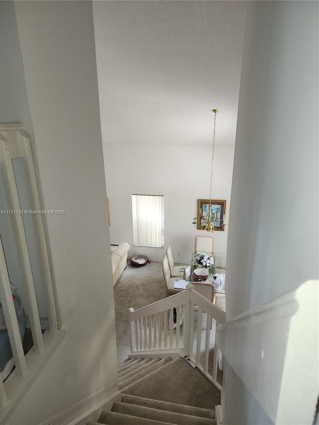 stairway with a textured ceiling, carpet floors, and a notable chandelier