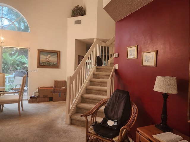 staircase with a high ceiling, visible vents, and carpet flooring