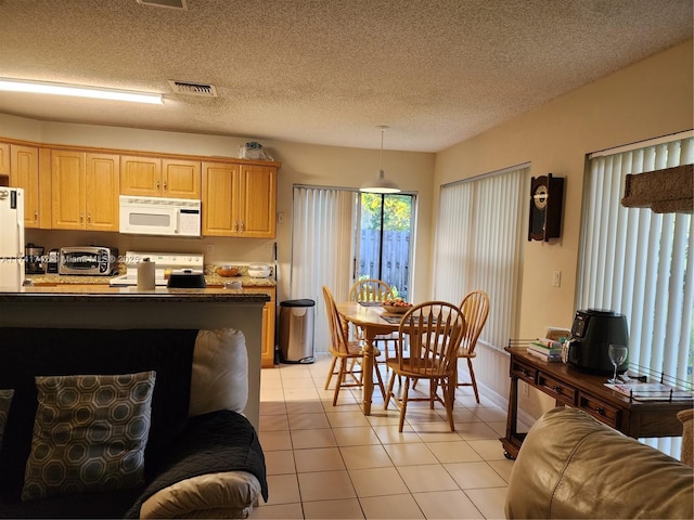 kitchen featuring visible vents, hanging light fixtures, white microwave, light tile patterned flooring, and range