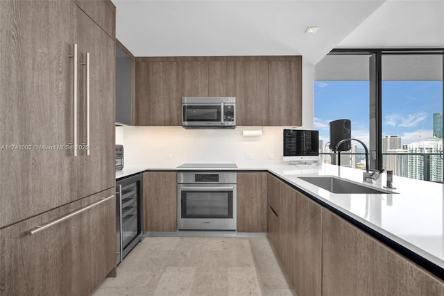 kitchen featuring beverage cooler, stainless steel appliances, a sink, light countertops, and modern cabinets