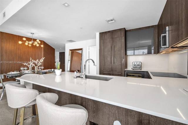 kitchen with black electric stovetop, light countertops, visible vents, stainless steel microwave, and a sink