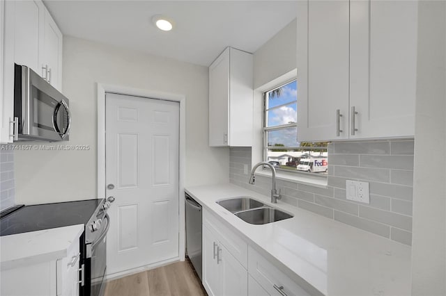 kitchen featuring sink, appliances with stainless steel finishes, white cabinetry, tasteful backsplash, and light wood-type flooring