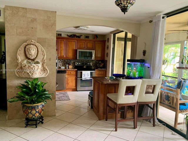 kitchen featuring tasteful backsplash, light tile patterned floors, crown molding, and stainless steel appliances