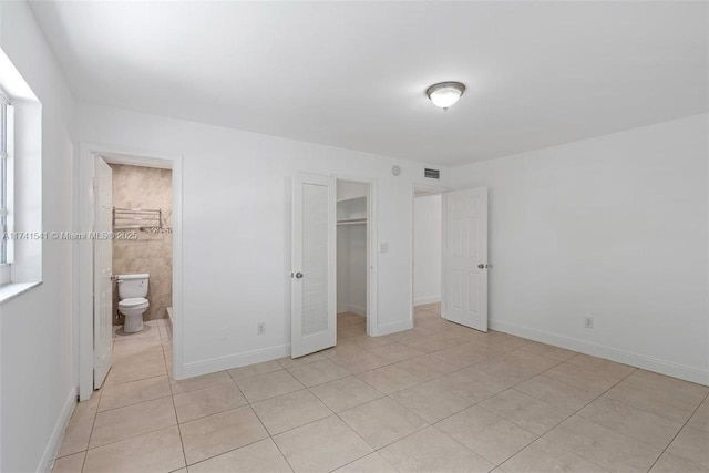 unfurnished bedroom with connected bathroom, light tile patterned floors, a spacious closet, and a closet