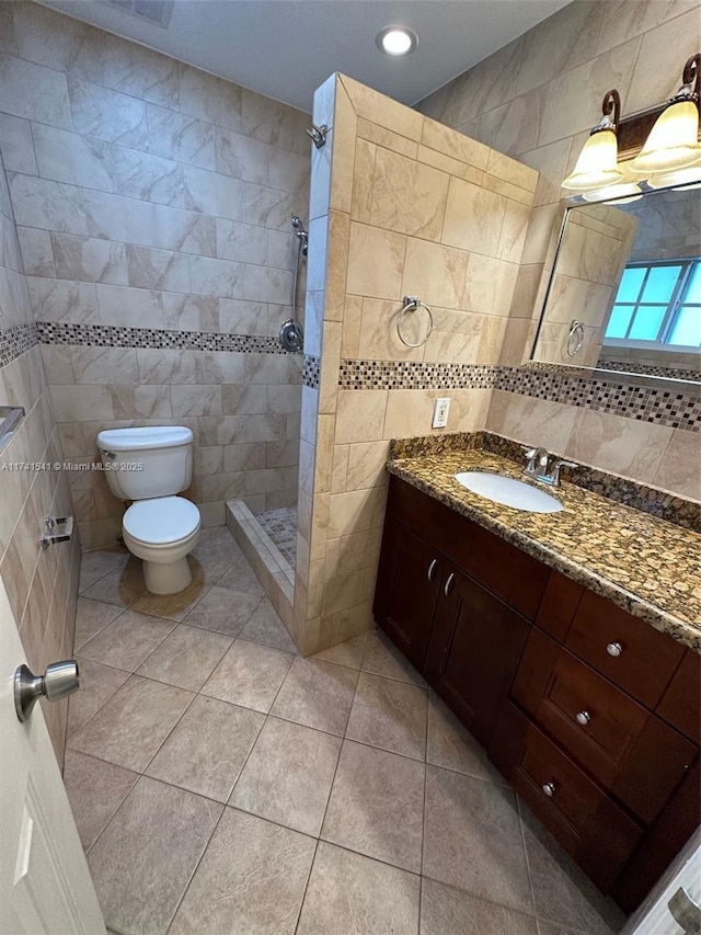 bathroom with tiled shower, toilet, tile walls, vanity, and tile patterned flooring