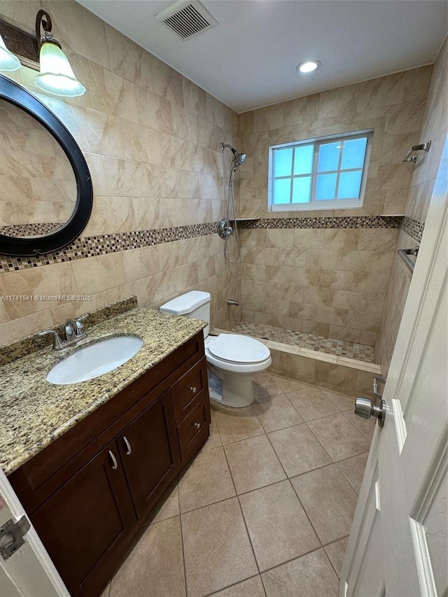 bathroom featuring tile walls, tile patterned flooring, vanity, tiled shower, and toilet