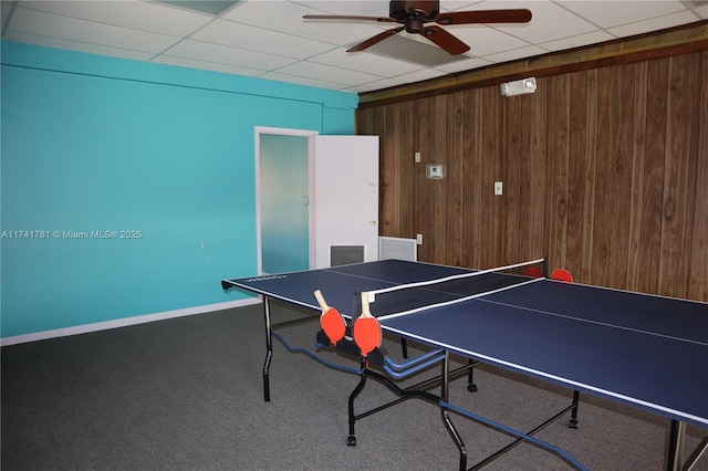 rec room with ceiling fan, carpet, a drop ceiling, and wooden walls