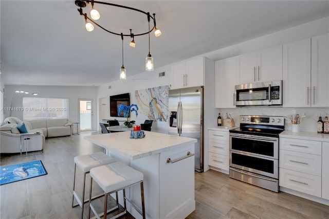 kitchen featuring a breakfast bar area, appliances with stainless steel finishes, a center island, light stone countertops, and white cabinets