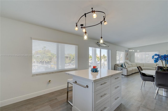 kitchen with a breakfast bar area, white cabinetry, hanging light fixtures, a kitchen island, and light hardwood / wood-style floors