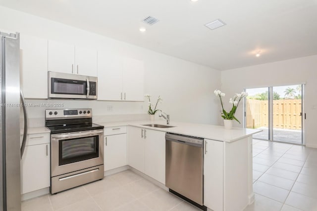 kitchen with sink, light tile patterned floors, appliances with stainless steel finishes, white cabinets, and kitchen peninsula